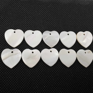 May include: Ten white heart-shaped shell charms with a hole for stringing. The charms are smooth and have a natural iridescent sheen.