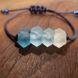 May include: A blue and white glass bead bracelet with a dark blue cord. The beads are hexagonal and fade from dark blue to white.
