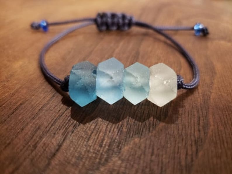 May include: A blue and white glass bead bracelet with a dark blue cord. The beads are hexagonal and fade from dark blue to white.
