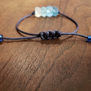 May include: A blue and white beaded bracelet with a navy blue cord and blue bead accents. The bracelet is tied with a knot.
