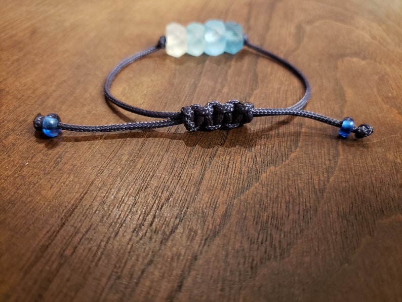 May include: A blue and white beaded bracelet with a navy blue cord and blue bead accents. The bracelet is tied with a knot.