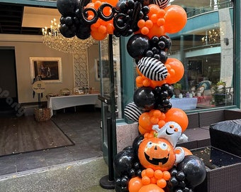 May include: A Halloween balloon arch with orange and black balloons. The arch is decorated with a ghost, a pumpkin, and the word "boo" in black letters.