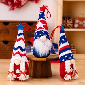 May include: Three patriotic gnome ornaments with red, white, and blue knit hats and bodies. The hats feature stars and stripes, and the gnomes have white beards and small noses. Each gnome has a red loop for hanging.