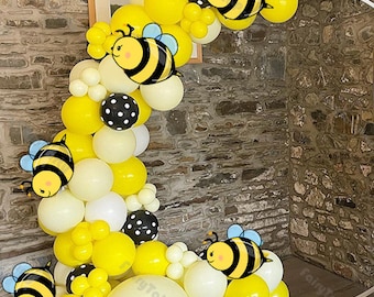 May include: A yellow and white balloon arch with black polka dot balloons and bee-themed balloons. The arch is decorated with yellow and white balloons and black polka dot balloons. The arch is decorated with bee-themed balloons.