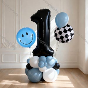 Pode incluir: Uma decoração de balões com o número um preto. Inclui um balão grande preto em forma do número um, um balão azul com um smiley, um balão quadriculado e vários balões azuis e brancos menores.
