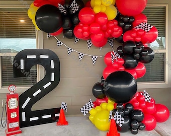 May include: A red and black balloon garland with checkered flags, a large black number 2 with a white road design, and a red gas pump with the number 66 on it.