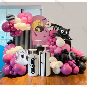 May include: A Halloween party decoration set with pink, white, and black balloons, a ghost balloon, a bat balloon, and a black and white striped backdrop. The backdrop has a pink and white moon with a black silhouette of a couple and a black and white striped pillar.
