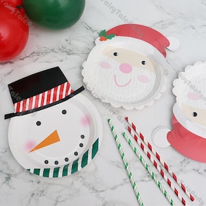 Puede incluir: Platos de papel con temática navideña con diseños de muñeco de nieve y Papá Noel. El plato del muñeco de nieve tiene un sombrero negro con rayas rojas y blancas, una nariz naranja y ojos de puntos negros. Los platos de Papá Noel tienen sombreros rojos.