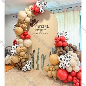 May include: A festive party decoration featuring a balloon arch in shades of brown, red, white, and cow-print balloons. A backdrop with a cowboy hat and the text "COWGIRL CANTOR'S hoedown" is also present. The theme is a cowgirl party.