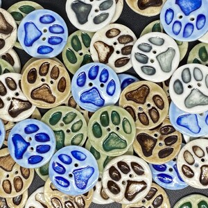 May include: Assortment of ceramic buttons with paw print designs in various colours, including blue, brown, green, and white.