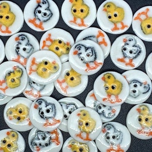 May include: A collection of ceramic buttons featuring various designs of chicks and birds. The buttons are white with colourful accents and are perfect for crafting projects.