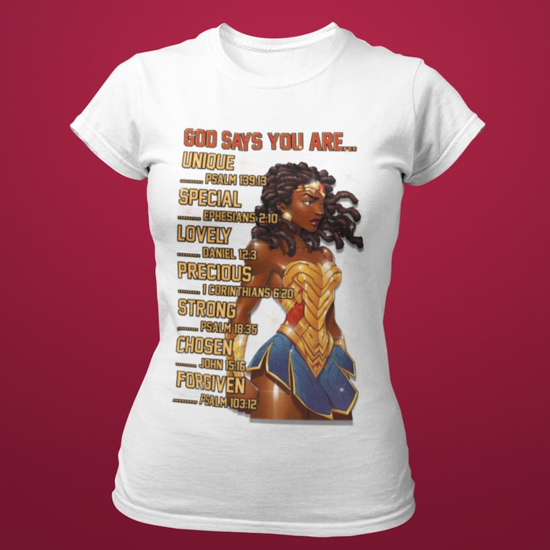 Puede incluir: Camiseta blanca con un gr&aacute;fico de una mujer de piel morena y cabello largo y rizado. La mujer lleva un traje de Wonder Woman. El texto "GOD SAYS YOU ARE..." est&aacute; impreso en la camiseta, junto con una lista de atributos positivos y vers&iacute;culos b&iacute;blicos correspondientes.
