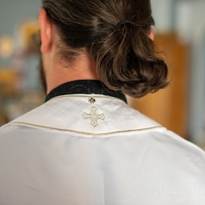 May include: A white clergy robe with a gold embroidered cross on the back of the collar.