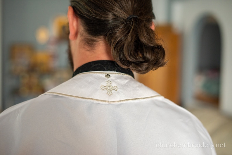 May include: A white clergy robe with a gold embroidered cross on the back of the collar.