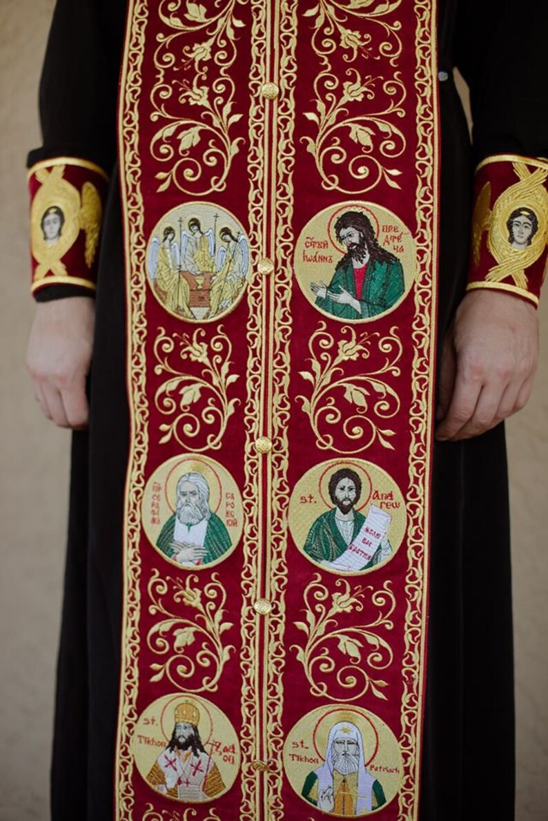 Pode incluir: Uma veste bordada em vermelho e dourado com m&uacute;ltiplos &iacute;cones religiosos, incluindo uma representa&ccedil;&atilde;o de Jesus Cristo, S&atilde;o Andr&eacute; e S&atilde;o Tikhon. A veste &eacute; decorada com padr&otilde;es florais intrincados.