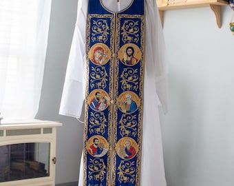Pode incluir: Uma veste litúrgica azul com bordados dourados e vários ícones religiosos. A veste é usada sobre uma túnica branca.