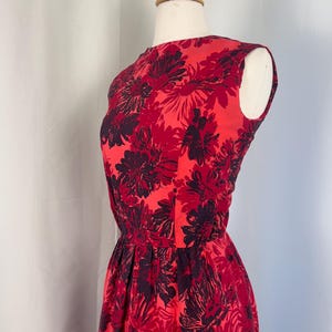 May include: A sleeveless red dress with a floral pattern in shades of red and dark purple. The dress has a fitted bodice and a flared skirt, displayed on a mannequin.