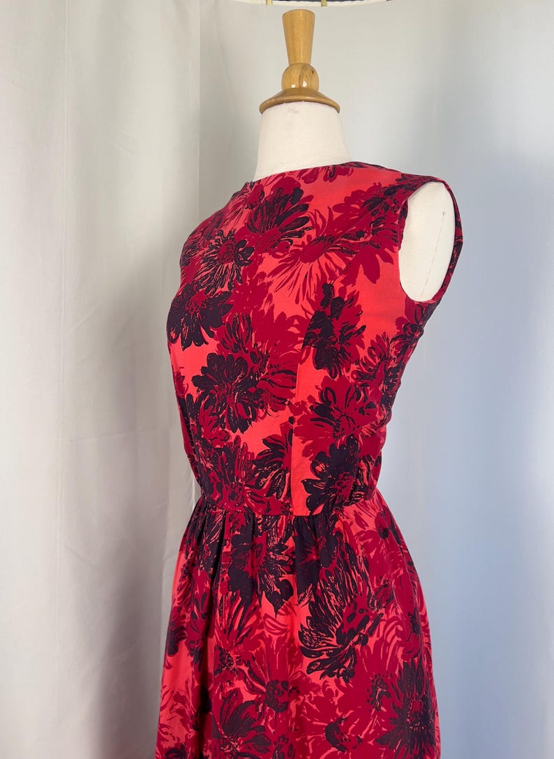 May include: A sleeveless red dress with a floral pattern in shades of red and dark purple. The dress has a fitted bodice and a flared skirt, displayed on a mannequin.