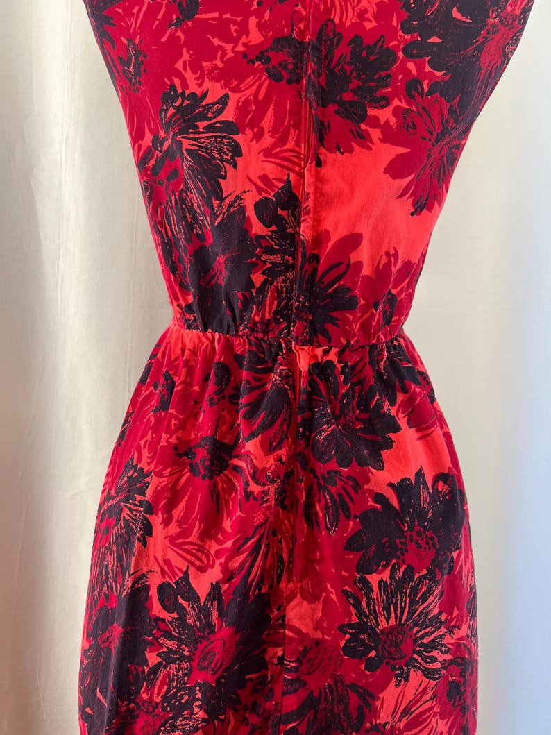 May include: A red dress with a black floral print. The dress features a fitted bodice and a gathered waist. The fabric looks lightweight, ideal for warmer weather. The dress is sleeveless.