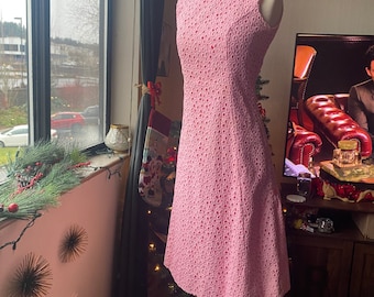 May include: A pink sleeveless dress with a delicate eyelet pattern. The dress is on a mannequin and has a fitted bodice and a flared skirt.
