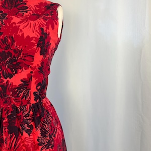 May include: A sleeveless red dress featuring a floral design in black and red. The dress is fitted at the waist and flares out. The fabric has a slight sheen.
