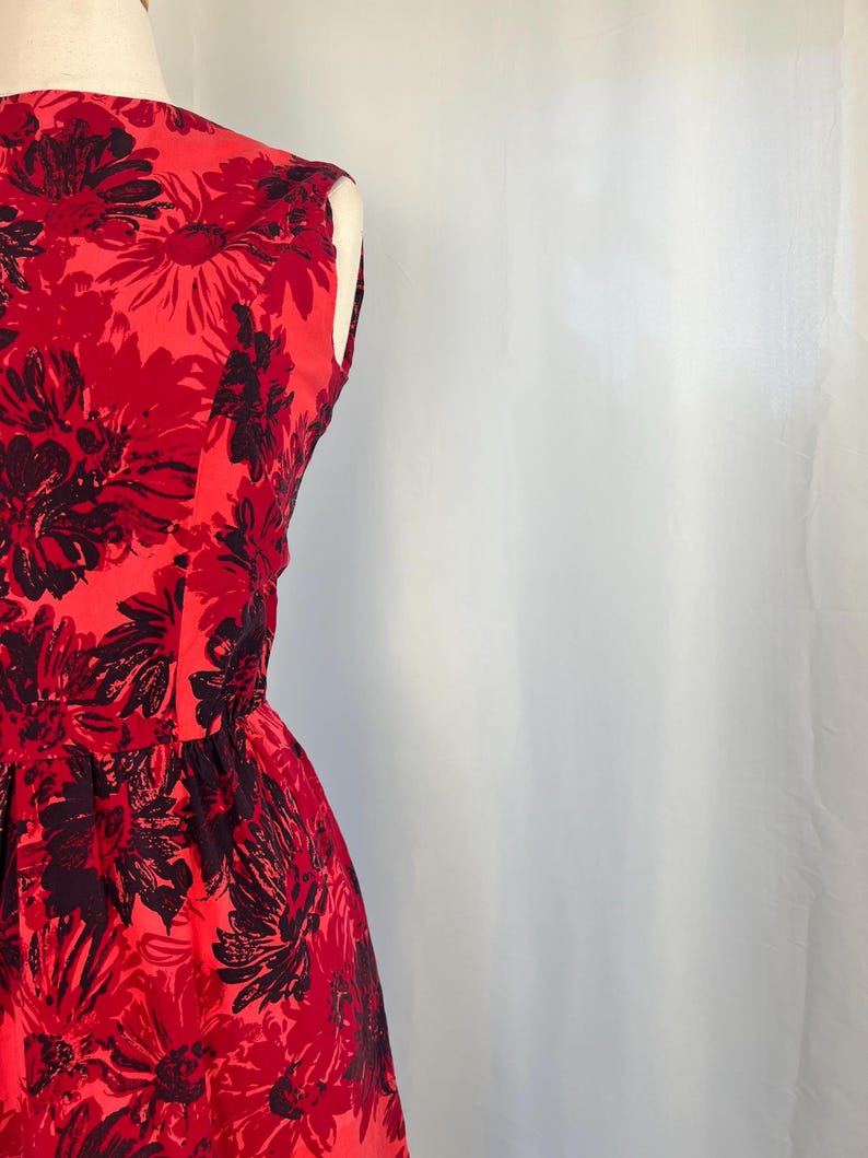 May include: A sleeveless red dress featuring a floral design in black and red. The dress is fitted at the waist and flares out. The fabric has a slight sheen.