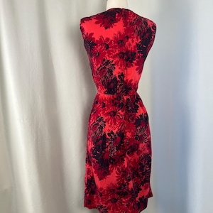 May include: A sleeveless red dress with a floral pattern in black and red hues. The dress is displayed on a mannequin, highlighting its fitted waist and knee-length hemline. The fabric looks lightweight, suitable for warmer weather. The dress is approximately 100 cm in length.