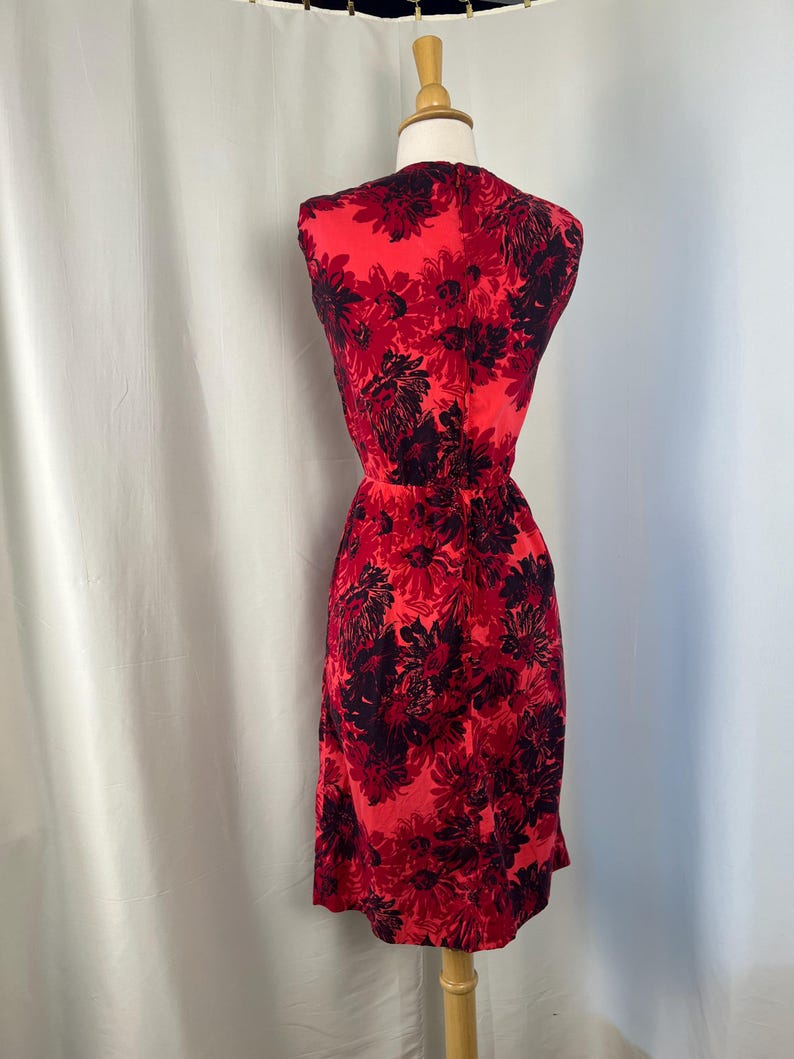 May include: A sleeveless red dress with a floral pattern in black and red hues. The dress is displayed on a mannequin, highlighting its fitted waist and knee-length hemline. The fabric looks lightweight, suitable for warmer weather. The dress is approximately 100 cm in length.
