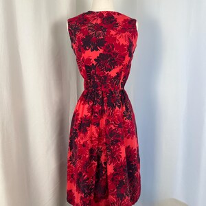 May include: A sleeveless red dress with a floral pattern in shades of red and dark purple. The dress has a fitted waist and a flared skirt, displayed on a mannequin.