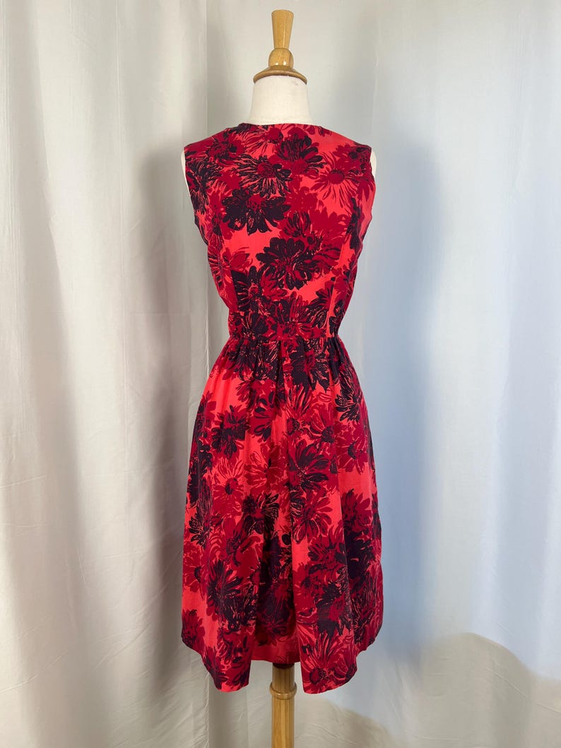 May include: A sleeveless red dress with a floral pattern in shades of red and dark purple. The dress has a fitted waist and a flared skirt, displayed on a mannequin.