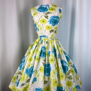 May include: A sleeveless dress featuring a white base with a vibrant floral print in shades of bright blue and lime green. The garment has a fitted bodice, a high neckline, and a full, pleated skirt that flares out from the waistline.