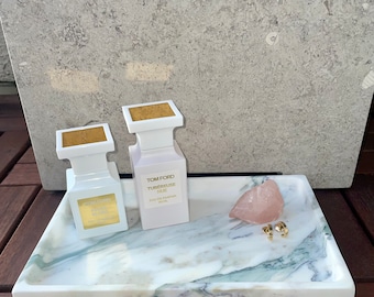 May include: A white marble tray with two white perfume bottles, one with the text "TOM FORD TUBEREUSE NUD", and a pink rose quartz crystal.