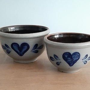 May include: Two stoneware bowls with blue and white heart designs. The larger bowl is slightly wider than the smaller bowl.
