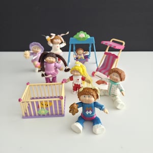 May include: A collection of vintage Cabbage Patch Kids dolls and accessories. The dolls are in various poses and outfits, with accessories including a swing set, stroller, and playpen. The dolls have painted faces and molded hair.