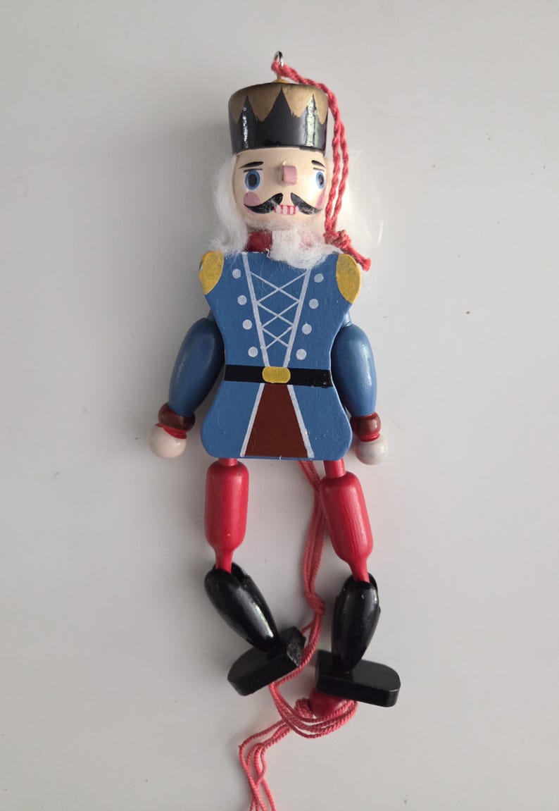 Peut inclure: Une d&eacute;coration casse-noisette en bois avec une couronne noire, des cheveux blancs et une veste bleue orn&eacute;e de d&eacute;tails de la&ccedil;age blancs. La figurine poss&egrave;de des cuisses rouges, des jambes noires et des pieds noirs, avec une ficelle rouge.