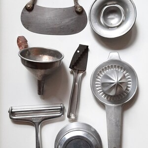 May include: A set of seven vintage kitchen tools made of metal. The tools include a funnel, a cheese grater, a citrus juicer, a pastry cutter, a citrus reamer, a pastry cutter, and a pastry cutter.