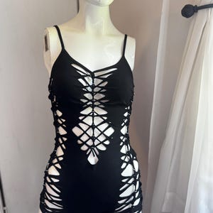 Könnte beinhalten: Schwarzer Overall mit einzigartigem Cut-Out-Design. Das einteilige Kleidungsstück hat dünne Spaghettiträger und ein Kreuzmuster über dem Oberteil und den Beinen. Der Stoff ist einfarbig schwarz und sorgt für einen kühnen und kantigen Look.