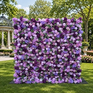 May include: A large, square floral wall backdrop densely covered in a variety of artificial flowers in shades of deep purple, violet, lavender, and light pink, interspersed with small green leaves, creating a solid, textured surface of blooms.