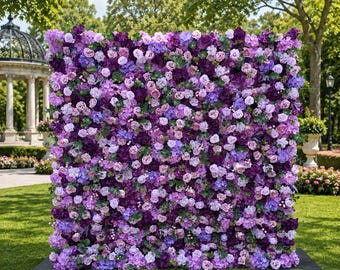 May include: A large, square floral wall backdrop densely covered in a variety of artificial flowers in shades of deep purple, violet, lavender, and light pink, interspersed with small green leaves, creating a solid, textured surface of blooms.