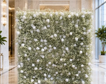 May include: A large, square floral wall backdrop composed of dense green baby's breath foliage interspersed with numerous white roses. The arrangement creates a uniform, textured surface of white blossoms and greenery, standing upright.