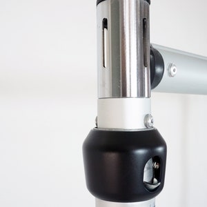 May include: Close-up of a silver and black adjustable support pole for a backdrop stand. The pole has a black plastic knob with a small hole for a pin.
