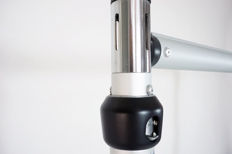 May include: Close-up of a silver and black adjustable support pole for a backdrop stand. The pole has a black plastic knob with a small hole for a pin.