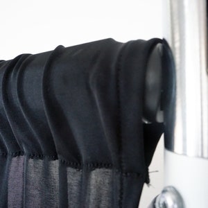 May include: Black sheer fabric backdrop hanging from a silver metal stand. The fabric is gathered at the top and hangs in soft folds.