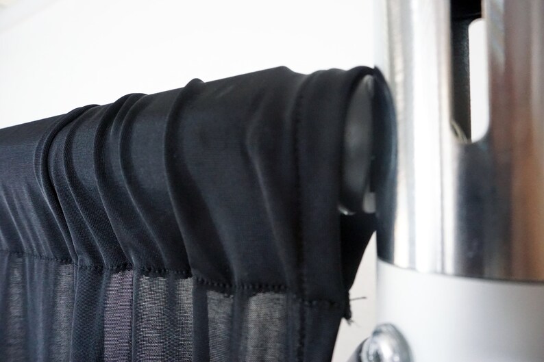 May include: Black sheer fabric backdrop hanging from a silver metal stand. The fabric is gathered at the top and hangs in soft folds.