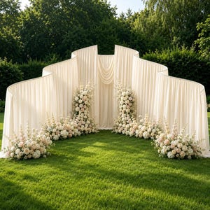 May include: A large, curved, off-white fabric backdrop featuring vertical pleats and draped fabric sections. The structure is decorated with multiple floral arrangements consisting of white and pale pink roses, hydrangeas, and tall spikes of flowers.