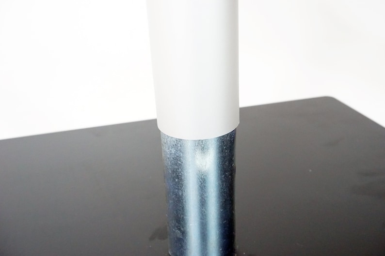 May include: Close-up of a white plastic cover on a silver metal table leg.