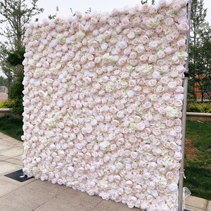 May include: A large white and blush pink artificial flower wall backdrop. The wall is made of many small roses and hydrangeas.