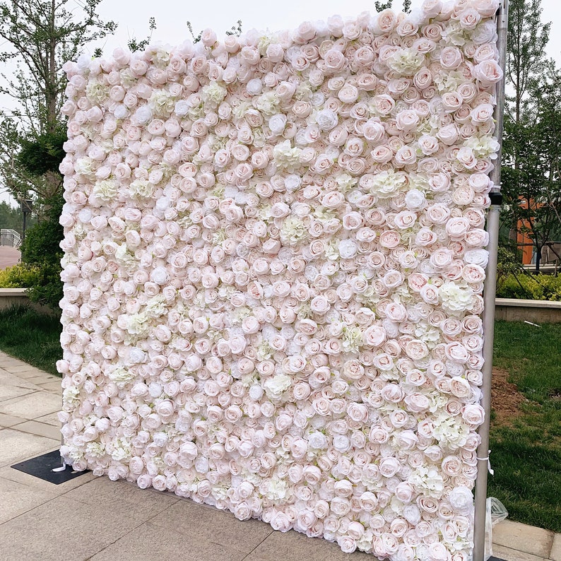 May include: A large white and blush pink artificial flower wall backdrop. The wall is made of many small roses and hydrangeas.