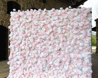 May include: A large, rectangular backdrop covered in artificial roses. The roses are a mix of white and pale pink, creating a soft, romantic aesthetic. The backdrop is supported by a silver metal frame, suitable for events.