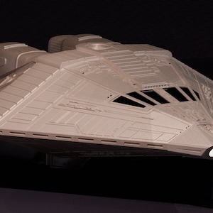 May include: A detailed model of a futuristic spaceship with a grey, textured exterior. The spaceship has a pointed nose and two large engines at the rear.